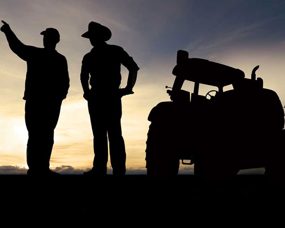 Two male farmers standing in front of a tractor silhouetted against a sunset