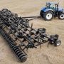 An aerial view of a Flexi-Coil 5000HD in a field being towed behind a blue New Holland tractor