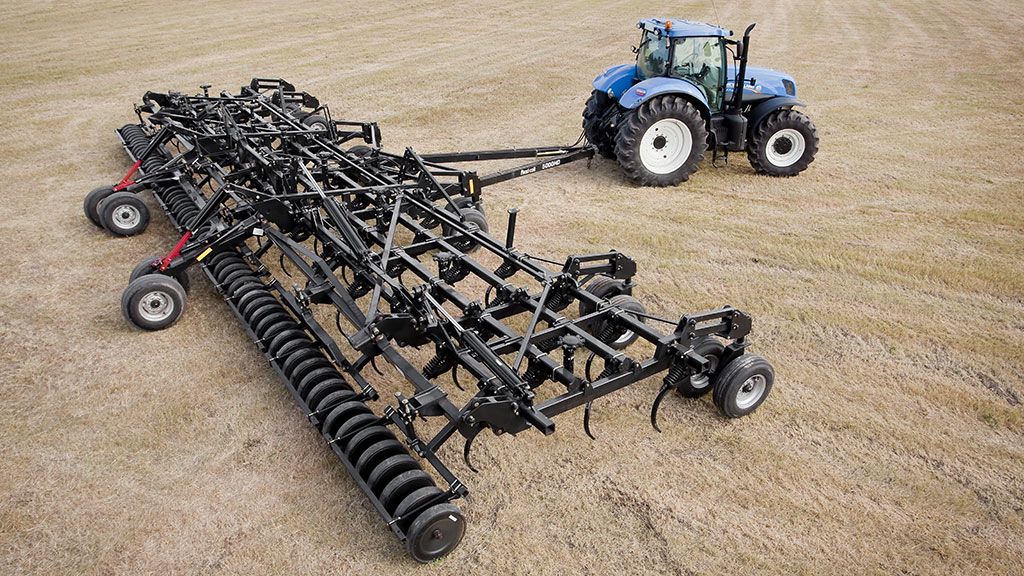 An aerial view of a Flexi-Coil 5000HD in a field being towed behind a blue New Holland tractor